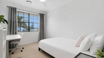 Habitación de hotel con cama, escritorio, silla, ventilador de techo y ventana con cortinas.
