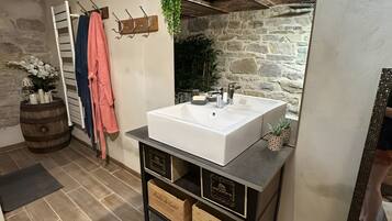 Une salle de bain avec un lavabo blanc, des meubles en bois, un porte-serviettes et un mur en pierre.
