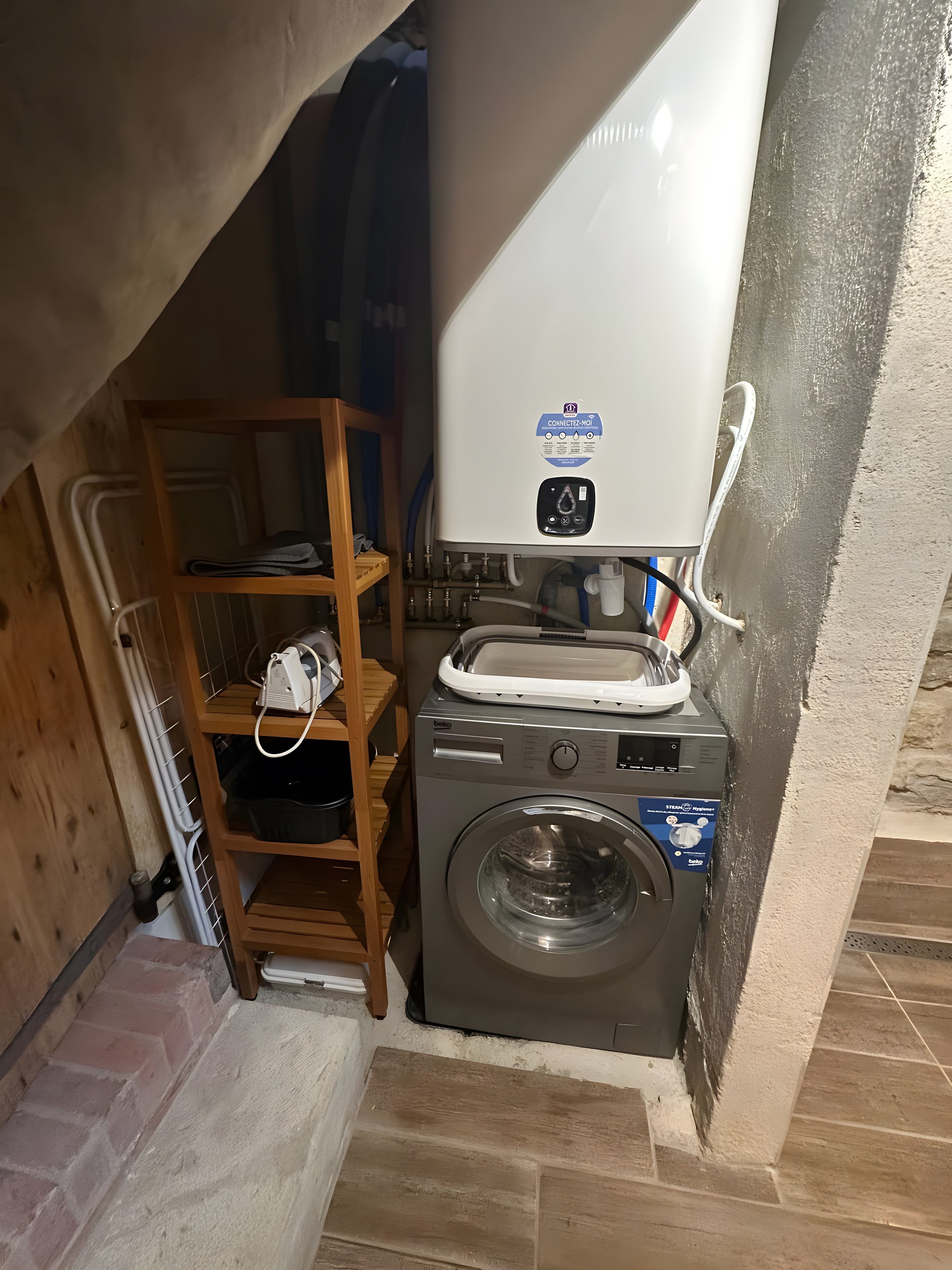 Un espace réduit dédié à la buanderie, comprenant un lave-linge, un étendoir et une étagère avec divers articles.