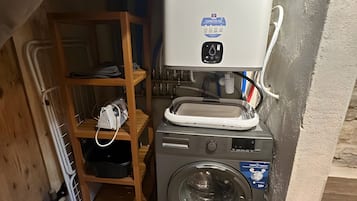 Un espace réduit dédié à la buanderie, comprenant un lave-linge, un étendoir et une étagère avec divers articles.