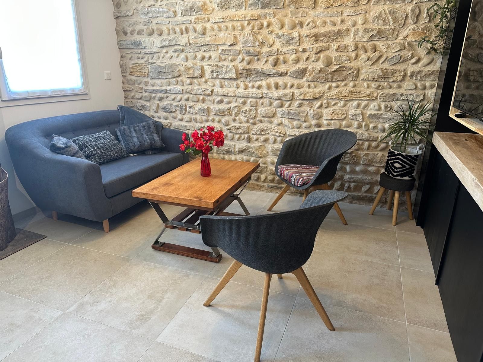 Un espace de vie moderne avec un mur en pierre, un canapé, une table basse, deux fauteuils et une petite plante.