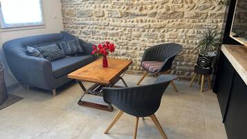 Un espace de vie moderne avec un mur en pierre, un canapé, une table basse, deux fauteuils et une petite plante.