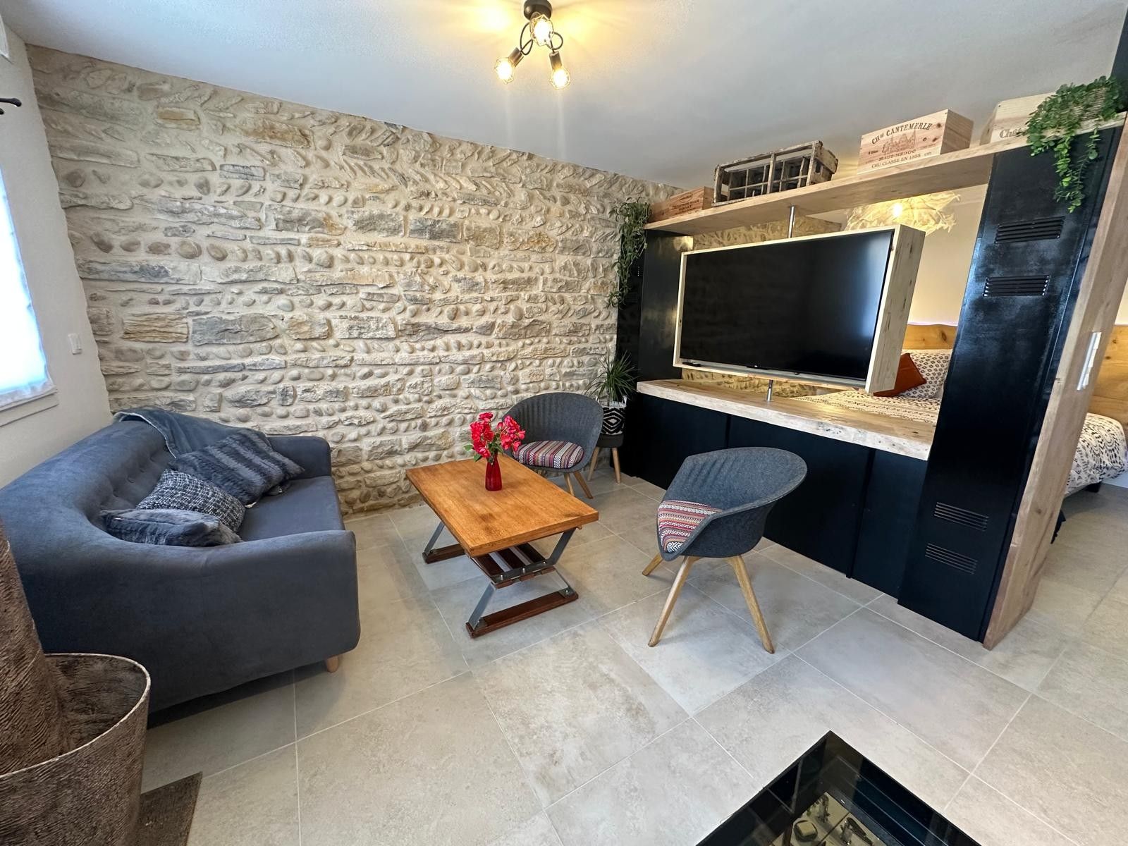Een moderne woonkamer met een stenen muur, een grijze bank, een houten salontafel en een flatscreen televisie.