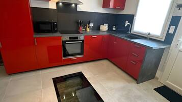 A modern kitchen with red cabinetry, a built-in oven, a microwave, and a window providing natural light.