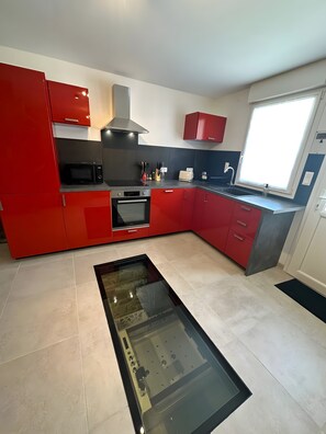A modern kitchen with red cabinetry, a built-in oven, a microwave, and a window providing natural light.