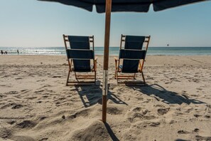 A beach with two wooden beach chairs under a blue umbrella. - North Myrtle Beach | Beach Escape | Pool & Ocean Access | 2BR Villa (North Myrtle Beach)