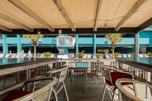 An outdoor bar area with multiple tables and chairs, a pool, and a view of a building with blue walls. - North Myrtle Beach | Beach Escape | Pool & Ocean Access | 2BR Villa (North Myrtle Beach)
