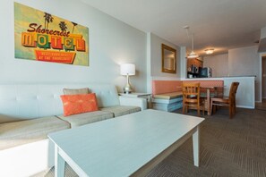 A motel room with a sofa, a dining table, a lamp, and a kitchen area. - North Myrtle Beach | Beach Escape | Pool & Ocean Access | 2BR Villa (North Myrtle Beach)