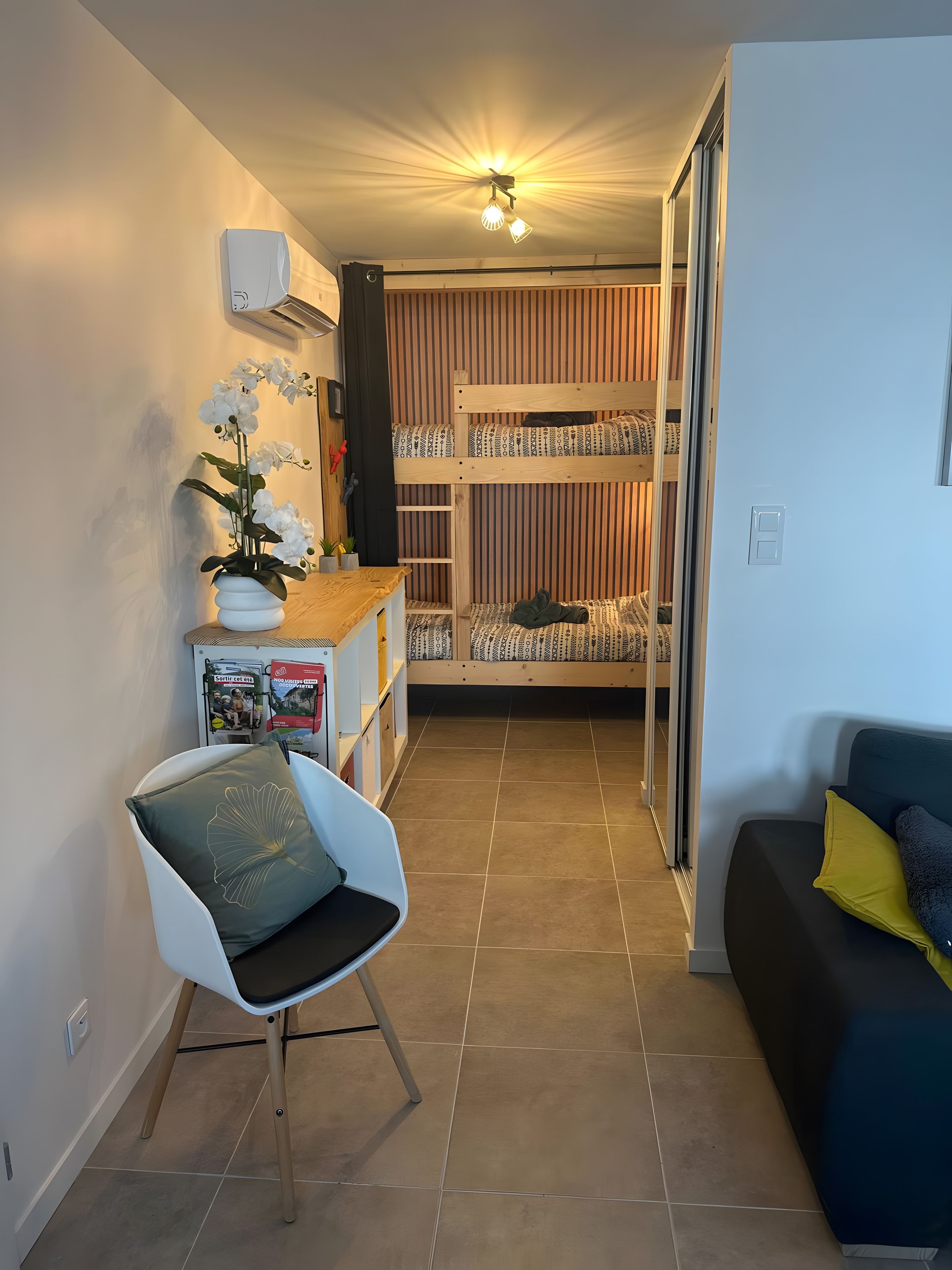 A compact living space with a bunk bed, a small seating area with a chair, and a potted plant.