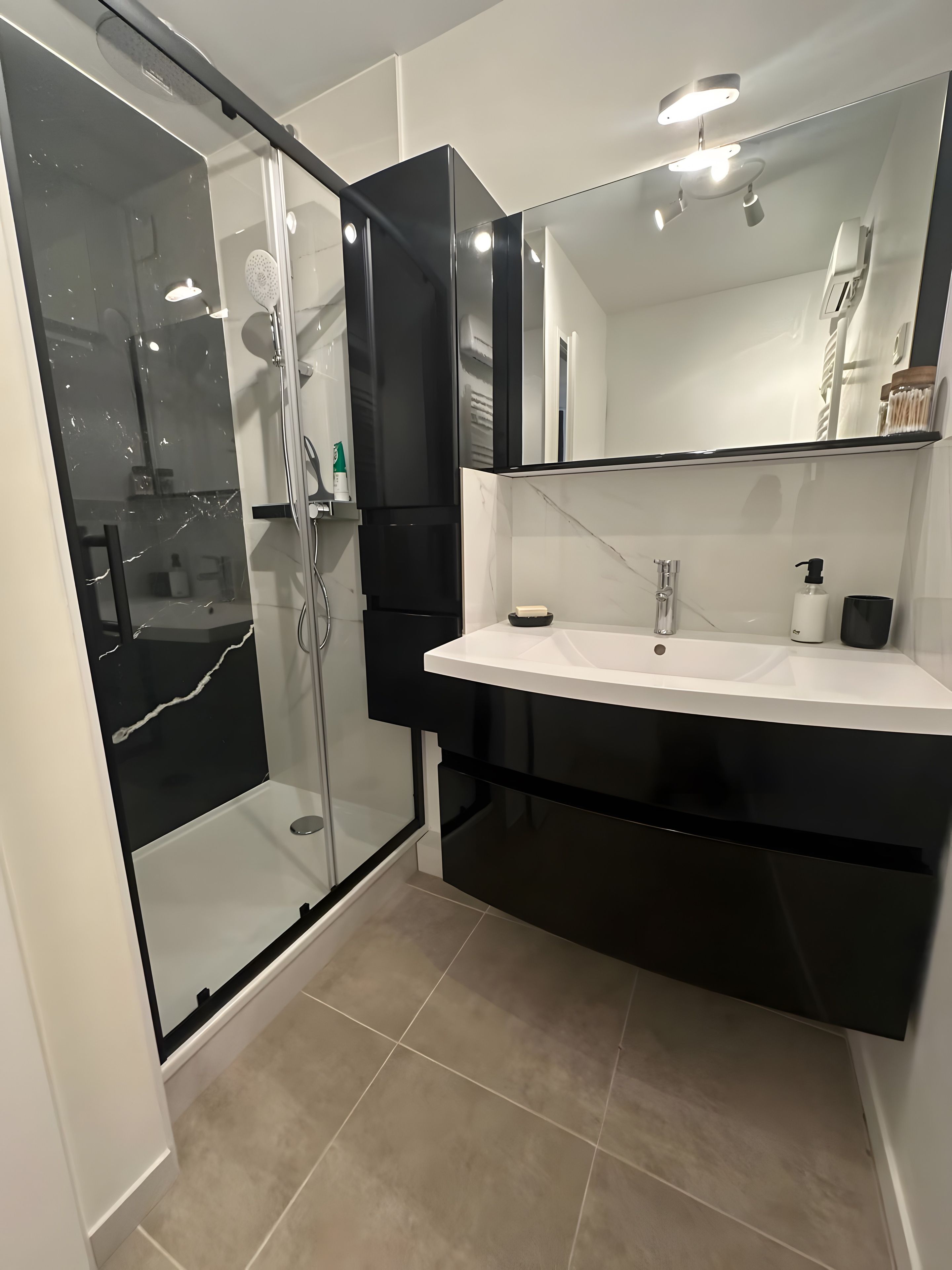 Une salle de bain moderne avec une douche à parois de verre, un lavabo blanc et un meuble-lavabo noir.