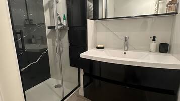 Une salle de bain moderne avec une douche à parois de verre, un lavabo blanc et un meuble-lavabo noir.
