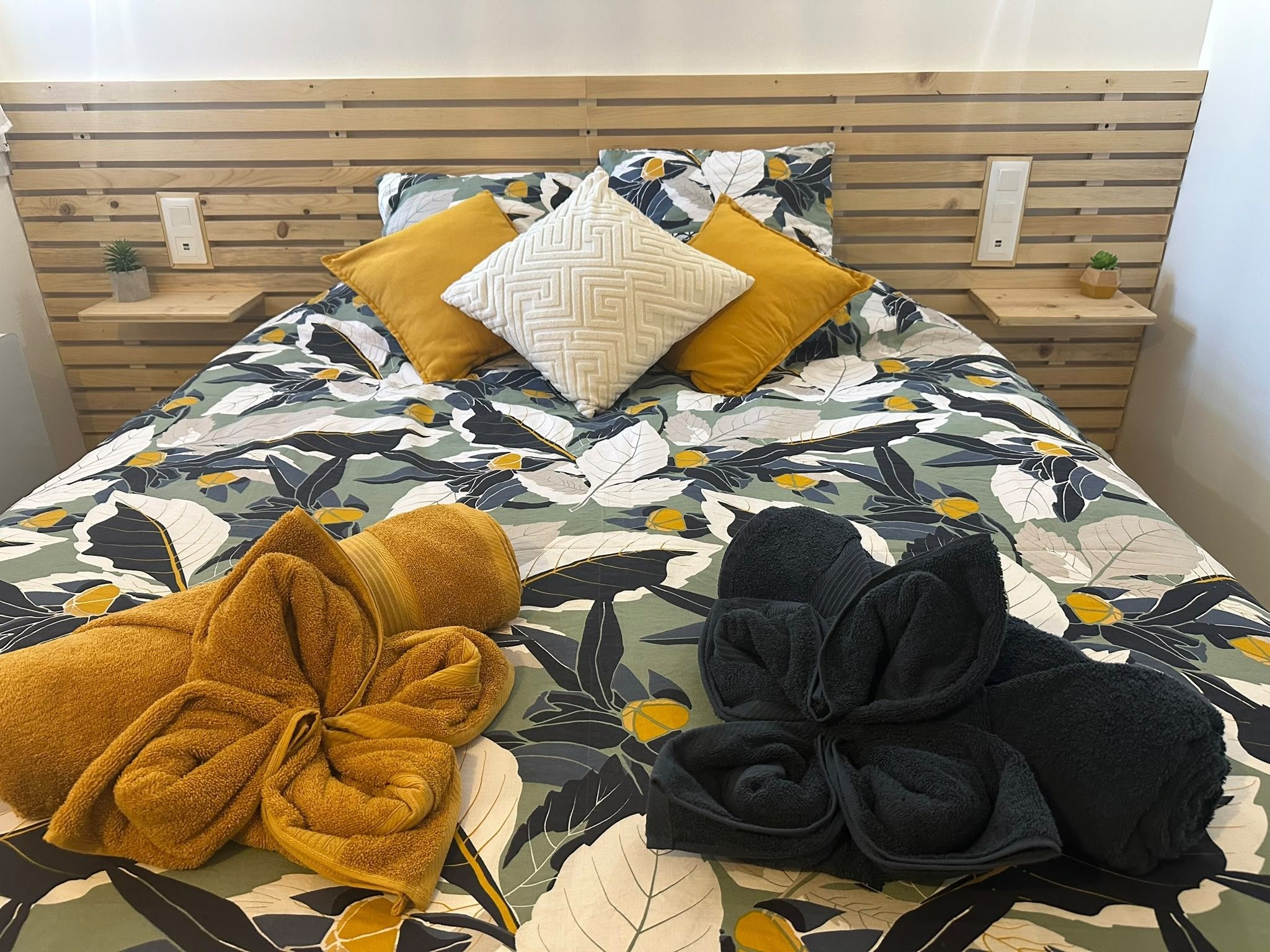 Un lit avec une couvre-lit à motifs floraux, deux oreillers et deux serviettes.