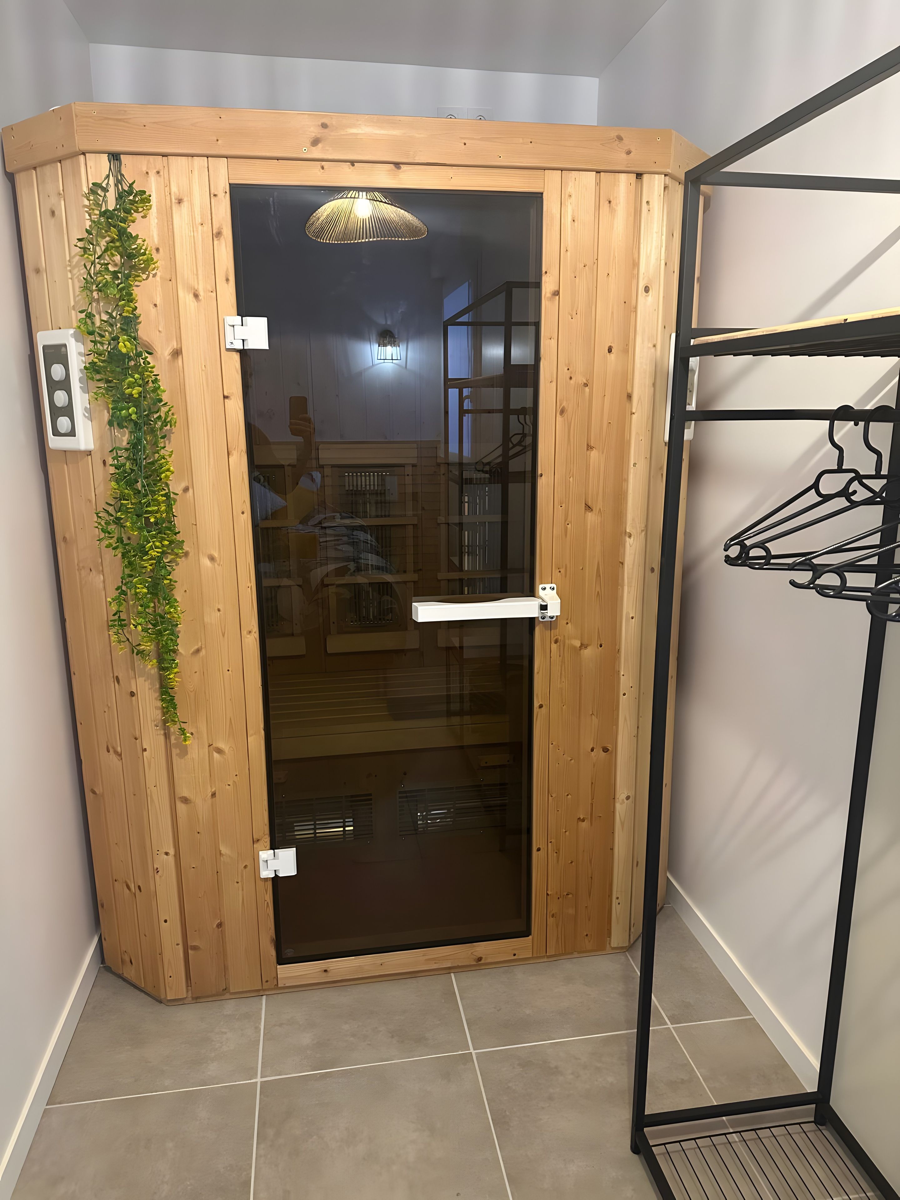 A corner room with a wooden door, a hanging plant, a white shelf, and a metal rack.