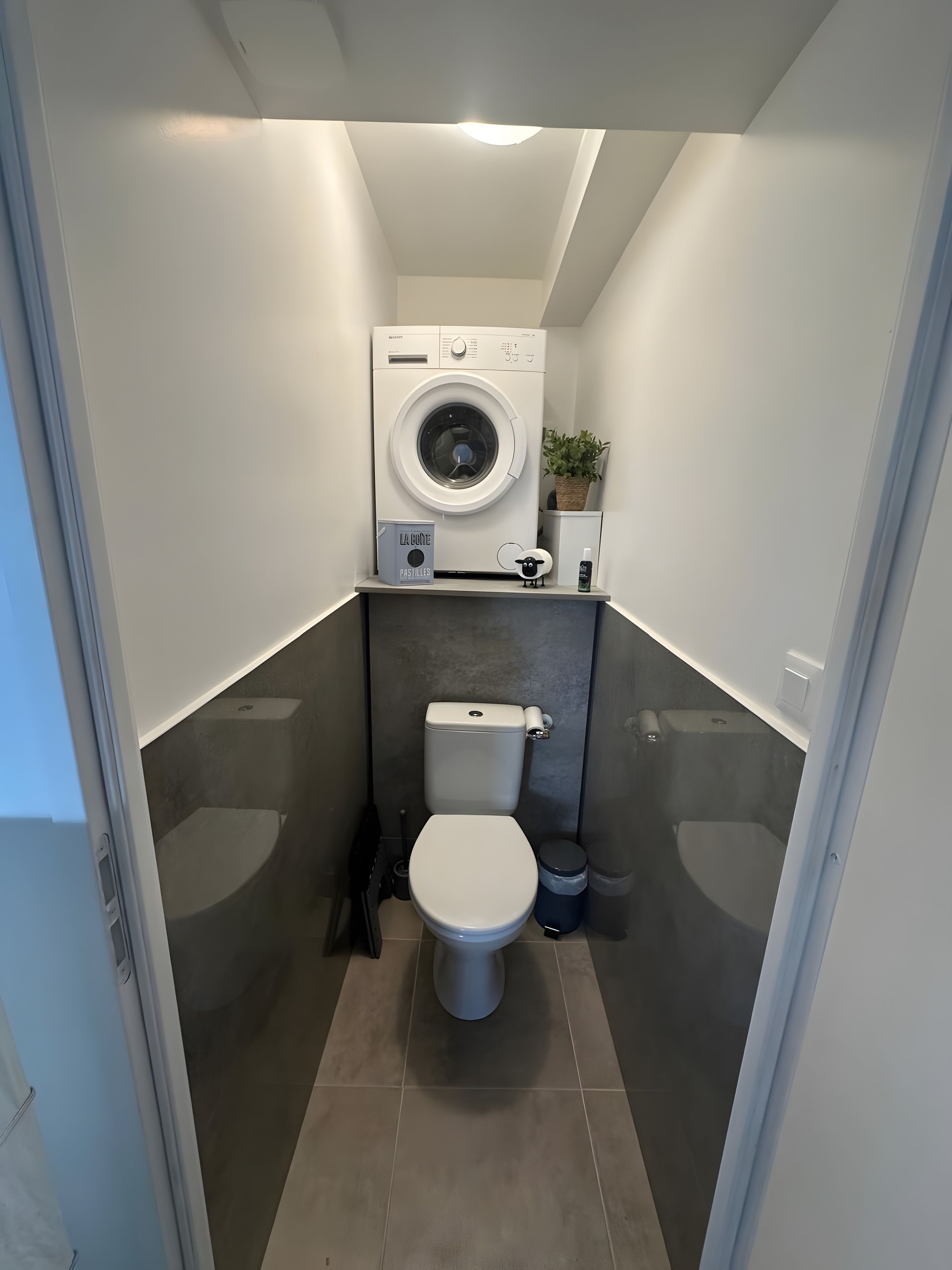 Une petite salle de bain équipée d’un lave-linge, de toilettes et d’une petite poubelle.