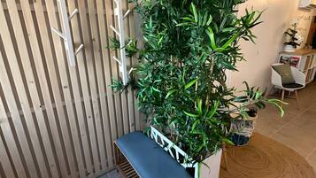 Un banc en bois avec un siège rembourré, un mur fait de lattes de bois verticales et une grande plante en pot aux feuilles vertes.