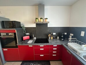 A compact kitchen with red cabinets, a microwave, an oven, a sink, and a dish rack. - Gîte Le Méridi’Ain Apartment in Viriat: 1 Bedroom, Private Sauna (Viriat)