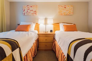 Een hotelkamer met twee bedden, een nachtkastje met een lamp, een klein tafeltje en kunst aan de muren.