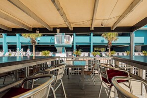 Een buitengedeelte met een bar, meerdere tafels en stoelen, een zwembad op de achtergrond en een overdekt zitgedeelte.