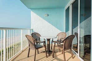 A balcony with a white railing, a round table, and four wicker chairs. - North Myrtle Beach | Oceanfront Stay | Pool & Beach | 2BR Villa (North Myrtle Beach)