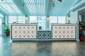 Ein Empfangsbereich mit modernem Design, der sich durch einen Fischgrätparkettboden, eine geometrisch gemusterte Trennwand und einen Blick auf die Stadt durch große Fenster auszeichnet.