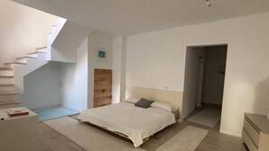 Quarto com cama, cabeceira de madeira, escada e uma pequena mesa.