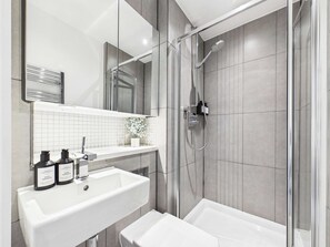 Un baño moderno con lavamanos, espejo y ducha blancos.