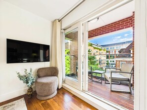 A balcony with a wooden floor, a chair, and a table. - Westminster 2BR Apartment with Balcony (Greater London)
