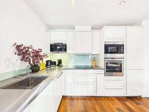 A modern kitchen with white cabinets, stainless steel appliances, and a wooden floor. - Westminster 2BR Apartment with Balcony (Greater London)