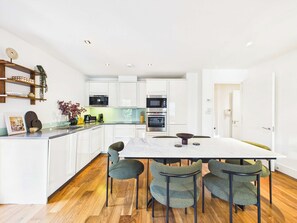 Una cocina moderna con armarios blancos, una isla central y un comedor con una mesa de mármol y cuatro sillas.