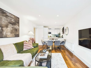 Uma sala de estar moderna com um sofá verde, uma mesa de centro e um espaço de jantar com mesa e cadeiras brancas.