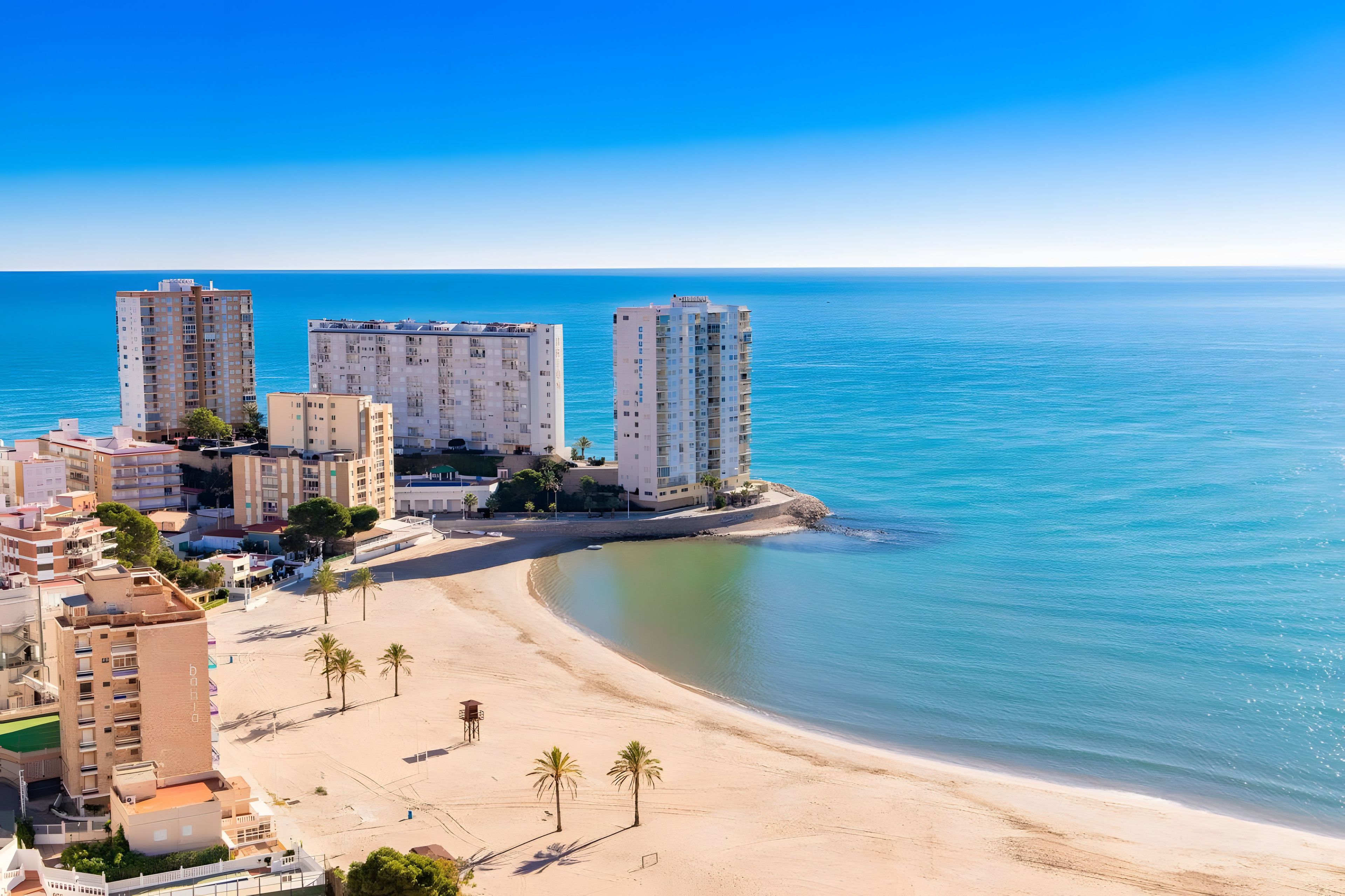 A coastal cityscape with high-rise buildings, a sandy beach, and clear blue waters.