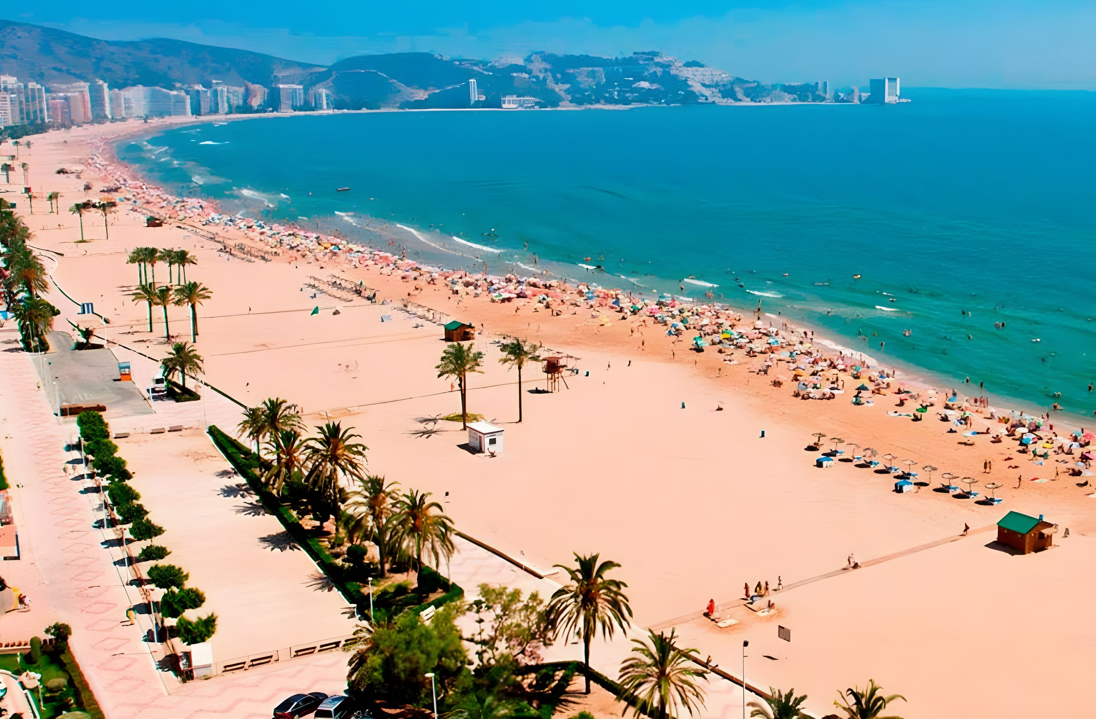 Una playa con palmeras, sombrillas y gente.