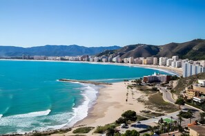 A coastal cityscape with a beach, buildings, and mountains in the background.