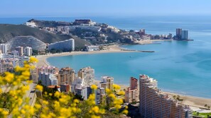 Paisagem costeira urbana com edifícios modernos, uma praia e mar azul cristalino.