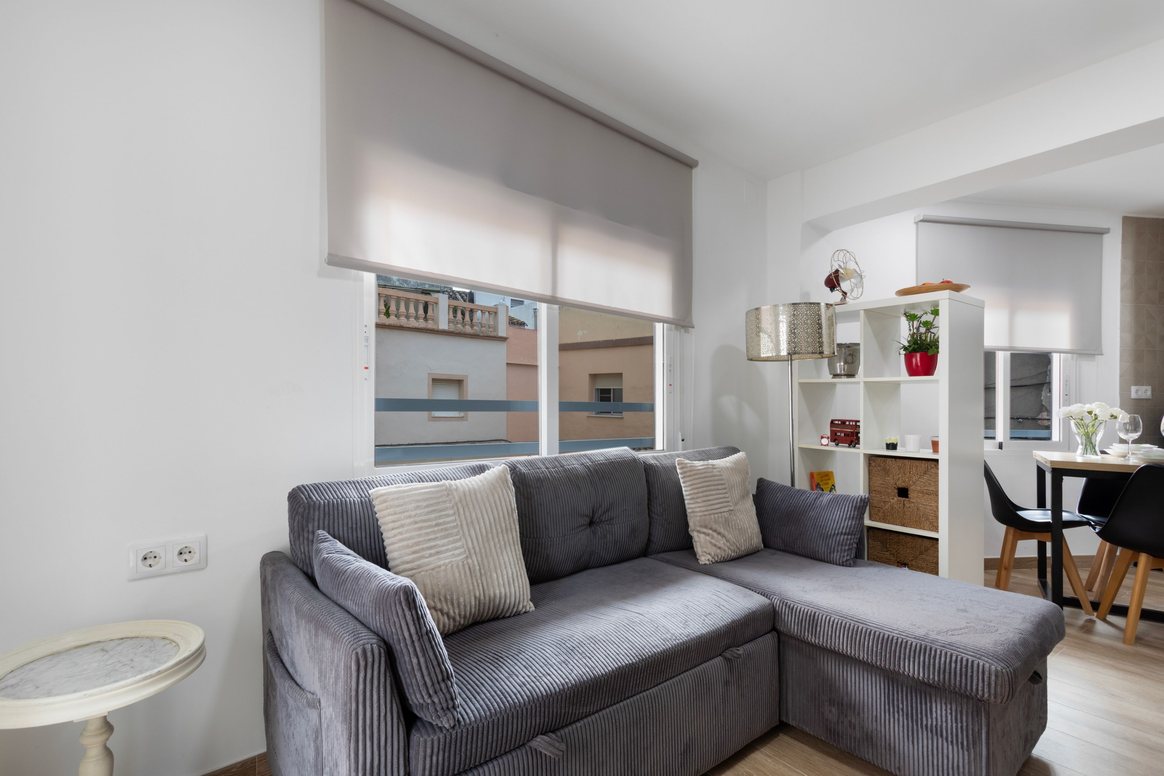 Una sala de estar moderna con un sofá seccional gris, una mesita redonda y una zona de comedor con una mesa y sillas de madera.