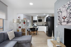 A modern living room with a grey sofa, a dining area with a table and chairs, a kitchen with a black refrigerator, and a large tiger mural on the wall.