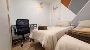 A bedroom with two beds, a desk with a chair, a standing fan, and a door with a 'HOME' sign. - Apartment 'Cullera' with Mountain Views, Wi-Fi, and Air Conditioning (Cullera)