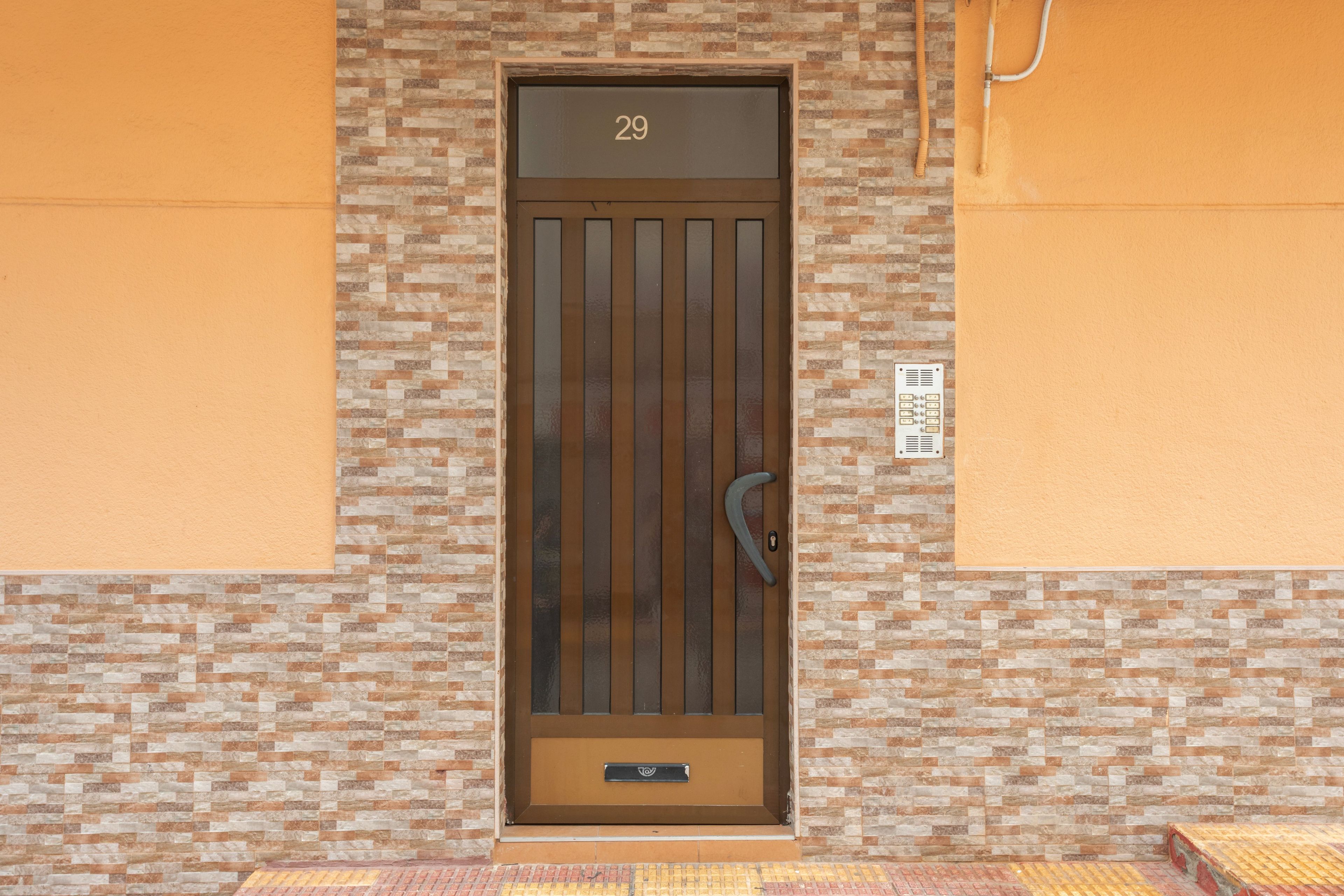 Una puerta con el número '29' encima, una mirilla y una pequeña placa con símbolos en la pared a la derecha.