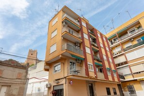 A multi-story residential building with balconies, air conditioning units, and a visible tower in the background.