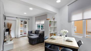 Una sala de estar moderna con un sofá gris, una mesa de comedor con sillas y una cocina al fondo.
