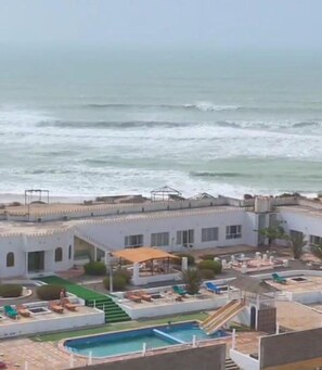 A coastal hotel with a pool, lounge chairs, and a view of the ocean.