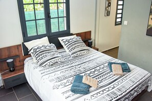 A bed with patterned bedding, a nightstand with a lamp, and a window with a view of greenery. - 4☆ Villa Thaïs – 3 Bedrooms – Private Pool - Guadeloupe ! (saint françois)