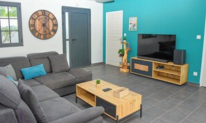 A modern living room with a grey sofa, a wooden coffee table, a TV on a wooden stand, and a clock on the wall. - 4☆ Villa Thaïs – 3 Bedrooms – Private Pool - Guadeloupe ! (saint françois)