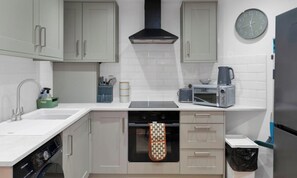 A modern kitchen with a dishwasher, oven, microwave, and a clock on the wall. - 2 Bed Flat in Airdrie | Sleeps 4 | Parking (Airdrie)