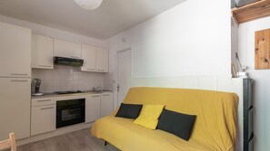 A compact kitchen with white cabinets, a stove, and a microwave. A yellow sofa with black cushions is positioned against the wall. - Cabin studio with nature view (Orcières)