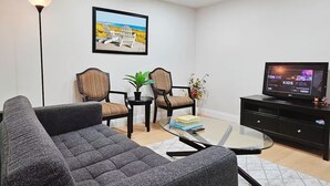 Uma sala de estar moderna com sofá, poltronas, mesa de centro, televisão e um quadro na parede.