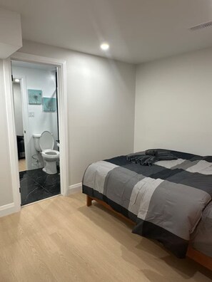Et soveværelse med seng, et badeværelse med toilet og en dør, der fører til et andet rum.