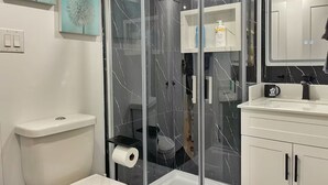 Uma casa de banho moderna com cabine de duche em vidro, sanita, lavatório com espelho e um armário com artigos de higiene pessoal.