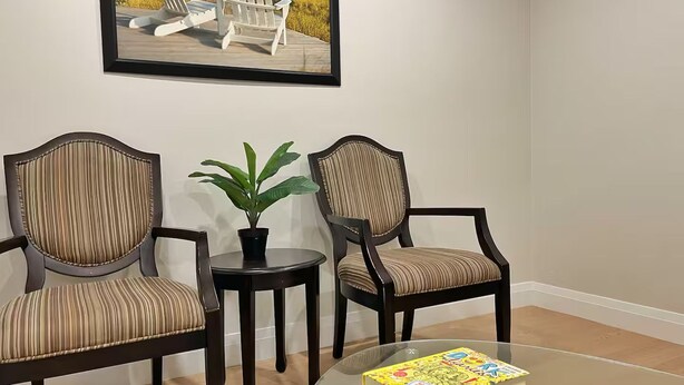 Um quarto com três cadeiras estofadas, uma pequena mesa com um vaso de planta e uma mesa de vidro com um livro.