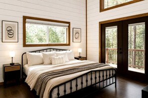 A bedroom with a bed, two bedside tables, a window, and a door leading to an outdoor area. - Luxury Cabin with Private Hot Tub & Sauna Getaway in Broken Bow, Oklahoma (Broken Bow)